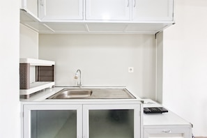 Uma cozinha compacta com uma pia de aço inoxidável, um micro-ondas e um pequeno móvel com gavetas.