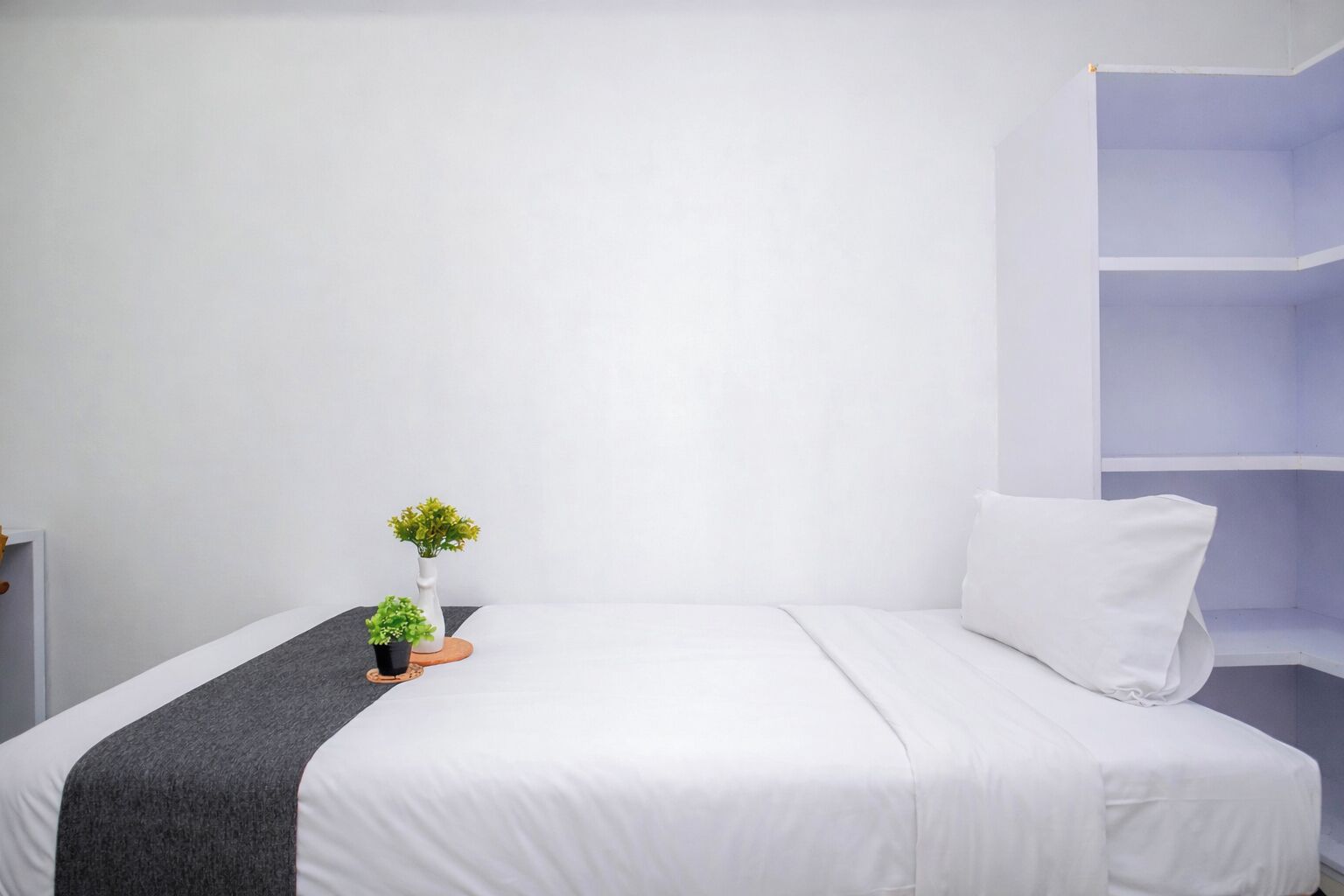 A single bed with white bedding, a grey throw, and a small potted plant on a wooden coaster.