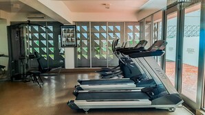 A gym with treadmills, a weight machine, and a glass wall with a view. - Bright And Comfy 2Br Apartment At Paddington Heights (Tangerang)