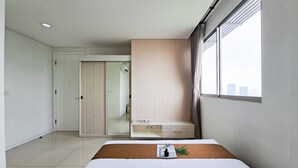 A modern hotel room with a bed, a desk, and a view of the city. - Bright And Comfy 2Br Apartment At Paddington Heights (Tangerang)