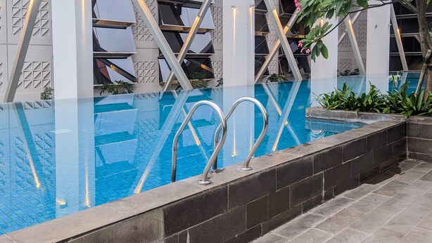 A modern indoor pool with clear glass walls, metal handrails, and a geometric architectural design. - Bright And Comfy 2Br Apartment At Paddington Heights (Tangerang)
