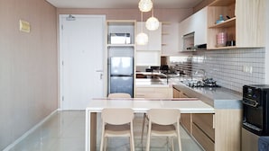 A modern kitchen with a central island, two chairs, a refrigerator, a stove, and a water dispenser. - Bright And Comfy 2Br Apartment At Paddington Heights (Tangerang)