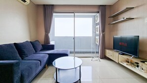 A modern living room with a sofa, a round coffee table, a TV, and a balcony with curtains. - Bright And Comfy 2Br Apartment At Paddington Heights (Tangerang)