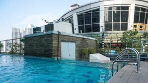 Ein Schwimmbecken mit Holzterrasse, einer Steinmauer und einem modernen Gebäude mit großen Fenstern im Hintergrund.