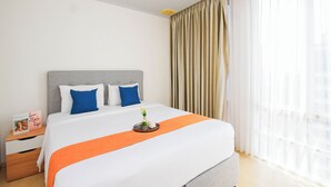 Ein Hotelzimmer mit einem Bett, einem Nachttisch, einer Ablage mit Blumen und einem Fenster mit Vorhängen.