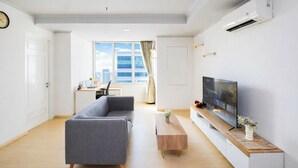 Ein modernes Wohnzimmer mit einer Couch, einem Couchtisch, einem Fernseher und einem Schreibtisch mit einem Laptop.
