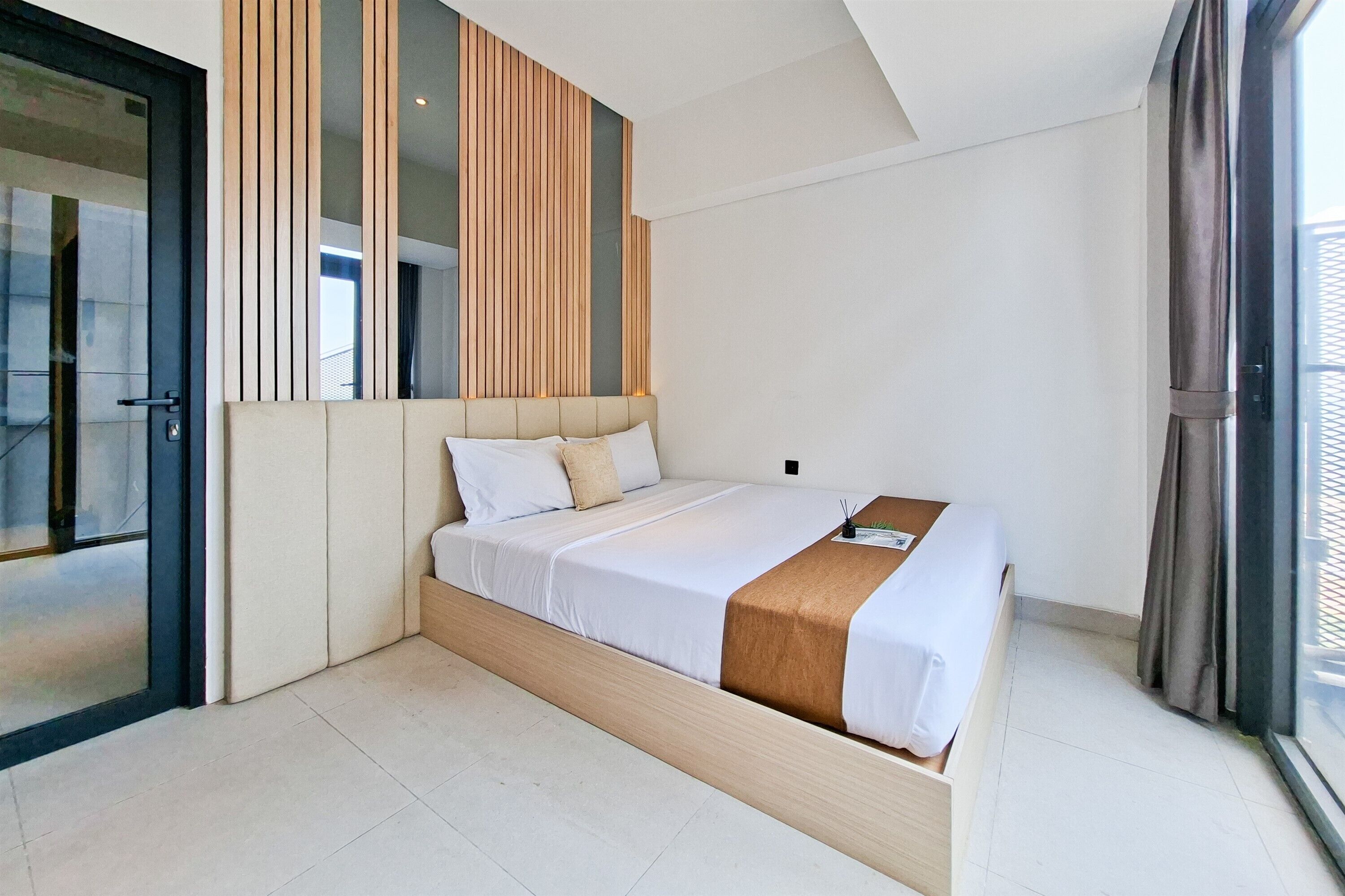 A modern hotel room with a bed, built-in wooden panel wall, and a sliding glass door.
