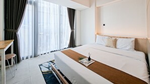 Une chambre d’hôtel moderne avec un grand lit, un bureau et une vue dégagée à travers des rideaux légers.