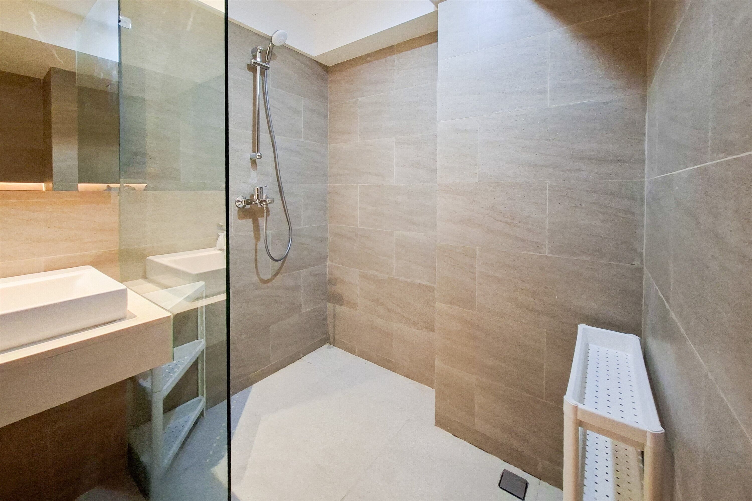 Ein modernes Badezimmer mit Duschkabine aus Glas, Waschbecken in Weiß und beige gefliesten Wänden.