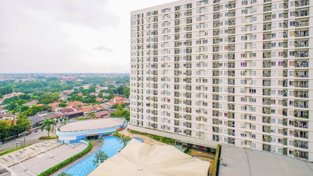 A high-rise building with multiple balconies, a swimming pool, and a view of a residential area. - Warm And Simple Studio At Cinere Bellevue Suites Apartment (Depok)