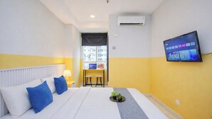 A hotel room with a bed, a desk with two chairs, a TV on the wall, and an air conditioning unit. - Warm And Simple Studio At Cinere Bellevue Suites Apartment (Depok)