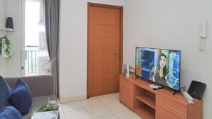 A living room with a TV, a wooden door, and a balcony. - Tranquil And Comfy 2Br At Cinere Bellevue Suites Apartment (Depok)