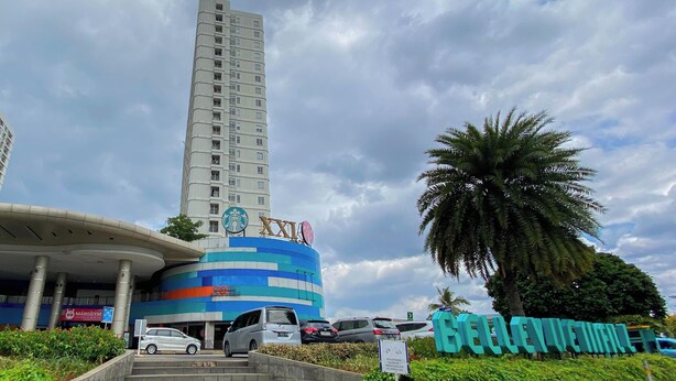 A tall building with a curved entrance and a palm tree in the foreground. - Tranquil And Comfy 2Br At Cinere Bellevue Suites Apartment (Depok)