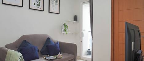 A living room with a sofa, a television, and framed botanical prints on the wall.