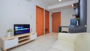 Un salon comprenant un téléviseur, un canapé, un meuble TV en bois et un coin cuisine avec une cuisinière.
