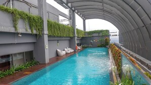 Una piscina con techo curvo, rodeada de vegetación y sillas de mimbre blancas.