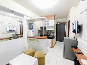 Ett kompakt bostadsutrymme med ett litet kök, en matplats med två pallar, en TV och en vattenautomat.