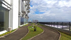 A pathway leading to a building with balconies, a fence, and a view of distant buildings. - Studio Apartment At Park View Condominium (Depok)