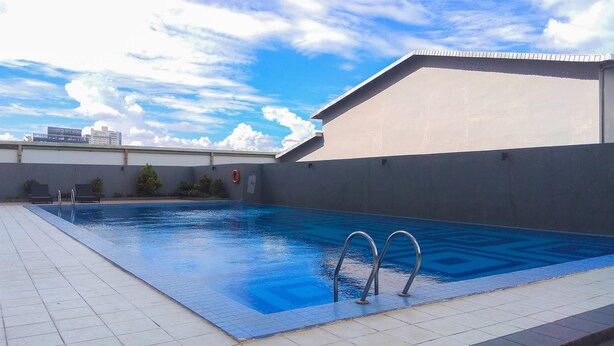 A swimming pool with metal ladders, a tiled deck, and a building with a flat roof in the background. - Studio Apartment At Park View Condominium (Depok)