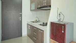 A kitchen with a dark door, wooden cabinets, a stainless steel sink, and a red appliance. - Studio Apartment At Park View Condominium (Depok)