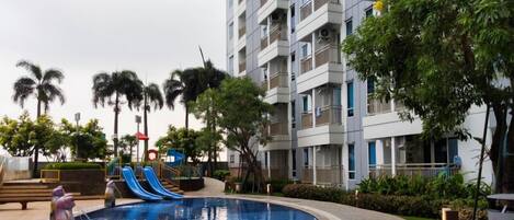 Un edificio residencial con balcones, piscina y zona de juegos para niños.
