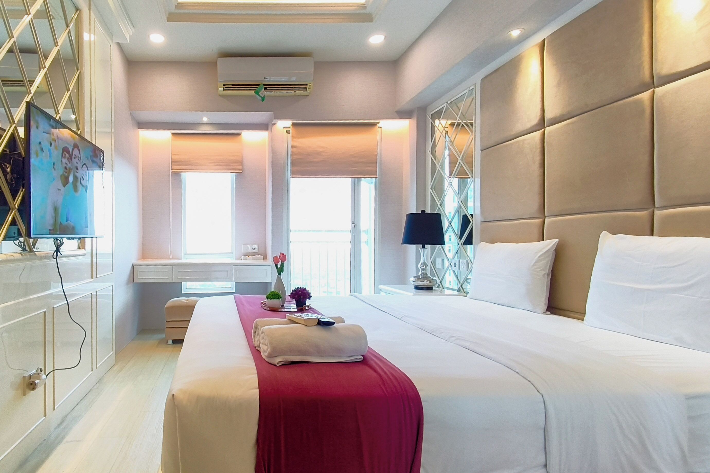 Habitación de hotel con una cama grande, un tocador con espejo, un televisor y una ventana con persianas.