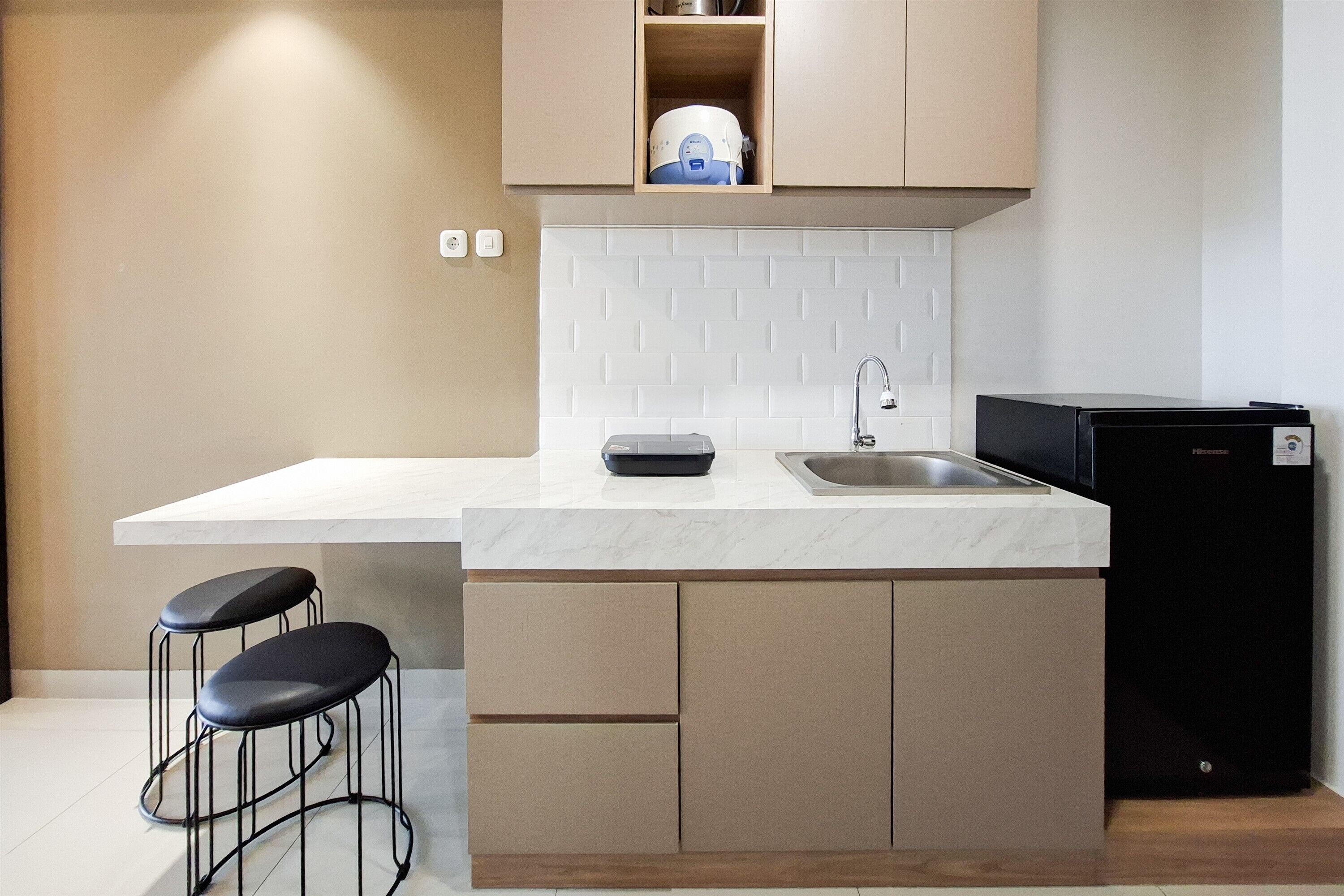 Eine moderne Küche mit Marmorarbeitsplatte, integriertem Spülbecken, einem schwarzen Kühlschrank und zwei Barhocker.