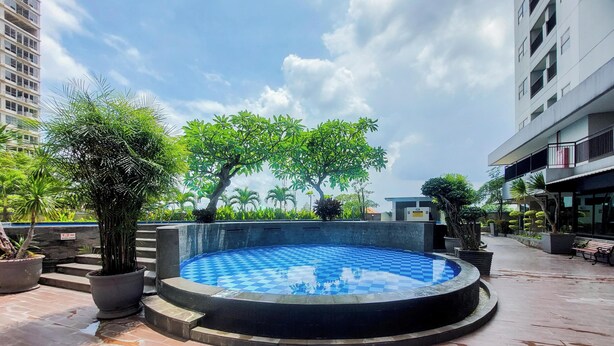 Una piscina en la azotea con diseño de cuadros, rodeada de plantas en macetas y un edificio con balcones.