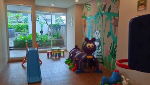 Zona de juegos infantiles con tobogán, taburetes de colores y un mural de animales.