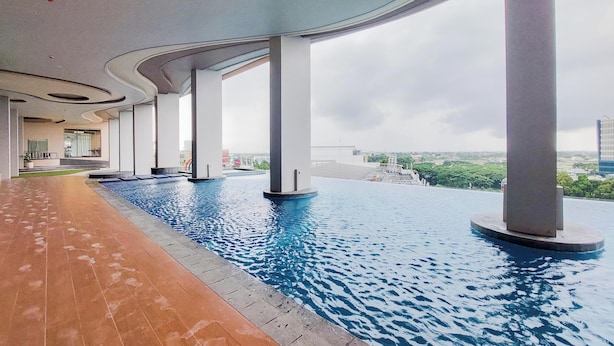 Ein Pool mit Endlosüberlauf auf dem Dach, mit Blick auf die Skyline der Stadt, gestützt von weißen Säulen, und einem mit Fliesen ausgelegten Weg links.
