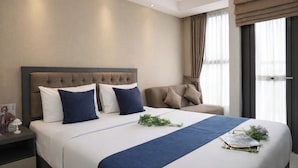 Ein Hotelzimmer mit einem großen Bett, einem Kopfteil, einem Nachttisch, einem Sessel und einem Fenster mit Vorhängen.