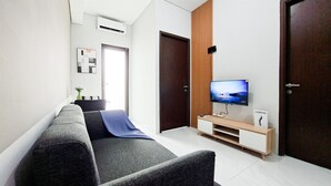 Una sala de estar moderna con un sofá, un televisor sobre un mueble de madera, una puerta y un aire acondicionado instalado en la pared.