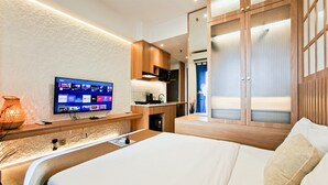 Quarto de hotel moderno com cama, televisão, escrivaninha e cozinha compacta.