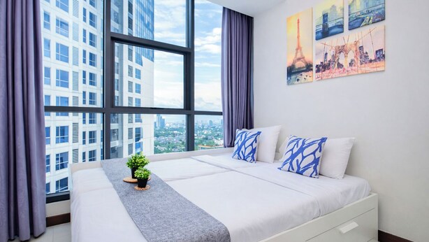 A modern hotel room with a large bed, a view of city buildings, and artwork on the wall. - Chic And Roomy 2Br Space At Apartment Casa Grande Residence (Jakarta)
