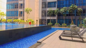 A modern building with a swimming pool, lounge chairs, and potted plants. - Chic And Roomy 2Br Space At Apartment Casa Grande Residence (Jakarta)