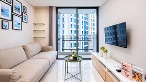 A modern living room with a sofa, a coffee table, a TV, and a bookshelf. - Chic And Roomy 2Br Space At Apartment Casa Grande Residence (Jakarta)
