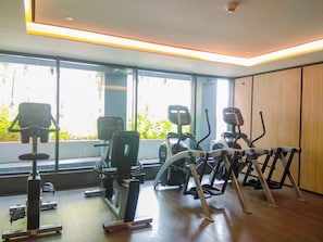 Ein Fitnessraum mit unterschiedlichen Trainingsgeräten, großen Fenstern und einer Holzwand.