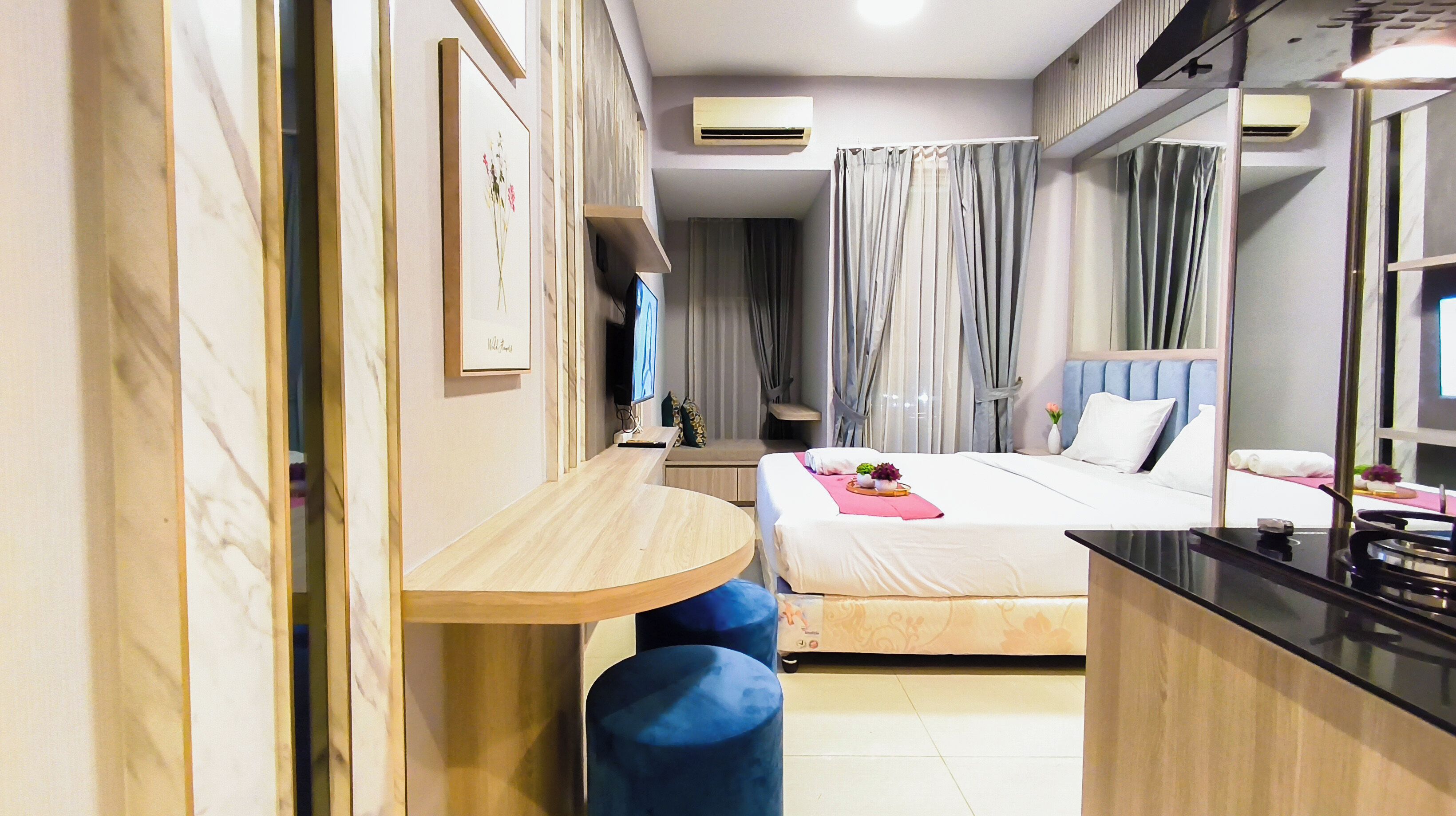 A hotel room with a bed, bedside table, a mirror, a TV, and a desk with a chair.