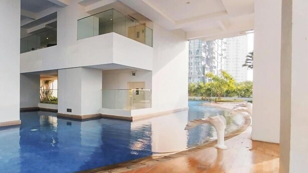 Une piscine intérieure moderne, dotée de rampes de protection en verre, d’un plancher en bois et offrant une vue sur les immeubles de grande hauteur.