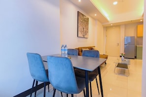 Ein moderner Essbereich mit Tisch, Stühlen und einer Couch. An der Wand hängt ein Gemälde, ein Kühlschrank steht dort und ein kleiner Tisch mit einer Vase ist ebenfalls zu sehen.