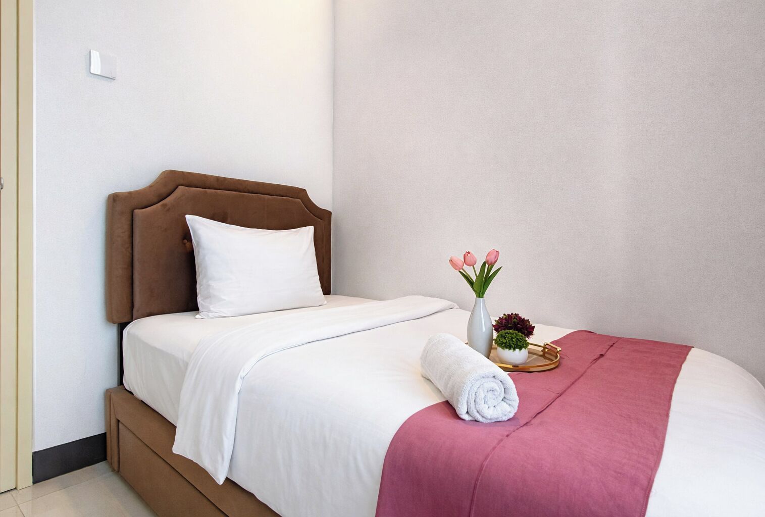 A neatly made bed with a brown headboard, white bedding, and a pink throw.