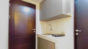 A compact kitchen with a dark wooden door, a white countertop, and a small sink. - Clean And Neat Deluxe Studio At Suncity Residence Apartment (Sidoarjo)