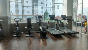 A gym with exercise equipment, large windows, and a view of residential buildings. - Clean And Neat Deluxe Studio At Suncity Residence Apartment (Sidoarjo)
