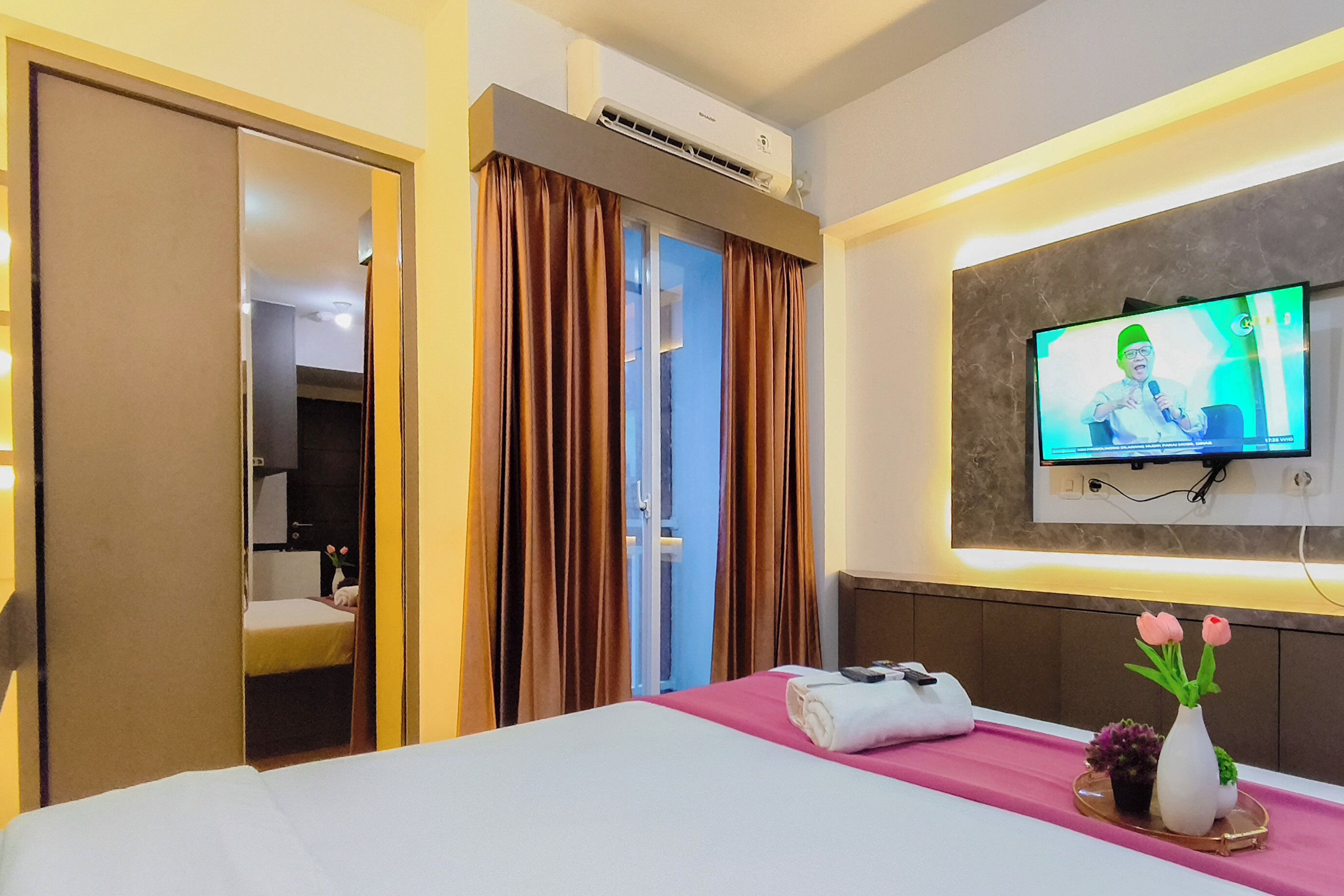 Habitación de hotel con cama, televisor montado en la pared, equipo de aire acondicionado y una puerta que da a otra habitación.