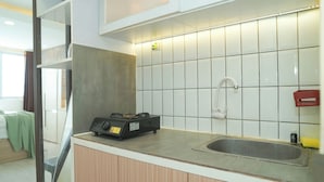 A kitchen with a gas stove, a sink, and a tiled backsplash. - Neat Studio At Amethyst Apartment Near Jiexpo (Jakarta)