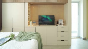 A modern hotel room with a bed, a TV, a desk with a computer, and a window. - Neat Studio At Amethyst Apartment Near Jiexpo (Jakarta)
