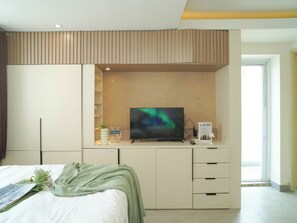 Ein modernes Hotelzimmer mit einem Bett, einem Fernseher, einem Schreibtisch mit Computer und einem Fenster.