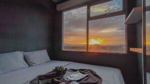 Una cama con sábanas blancas, una manta oscura y una planta pequeña a un lado.