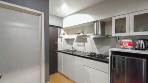 Una cocina compacta con armarios blancos, un refrigerador de acero inoxidable, una estufa a gas y una tetera.