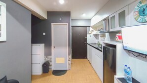 Cocina compacta con refrigerador, estufa y microondas. Hay una puerta que da a otra habitación y un pequeño basurero.